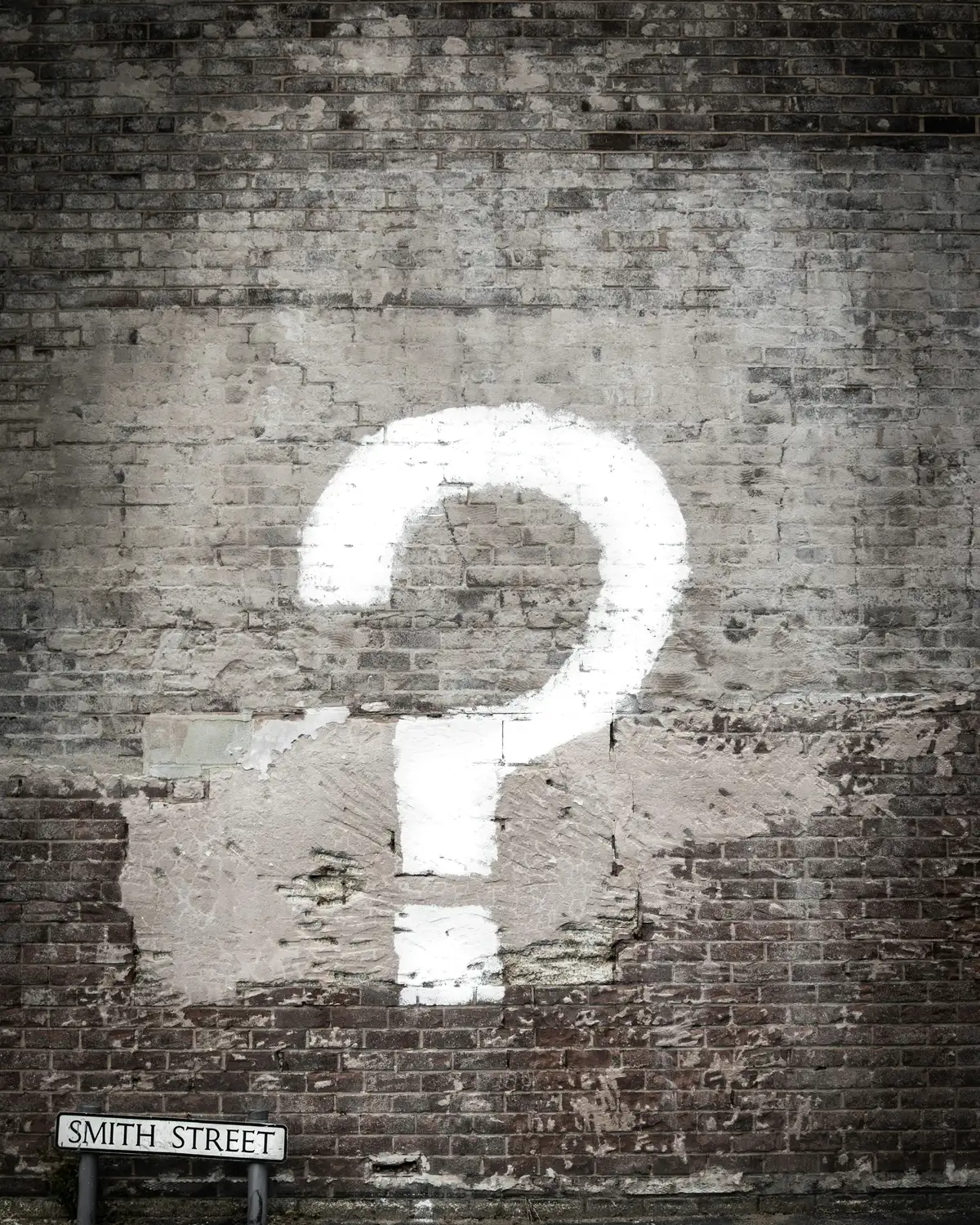 A white question mark painted on a brick wall